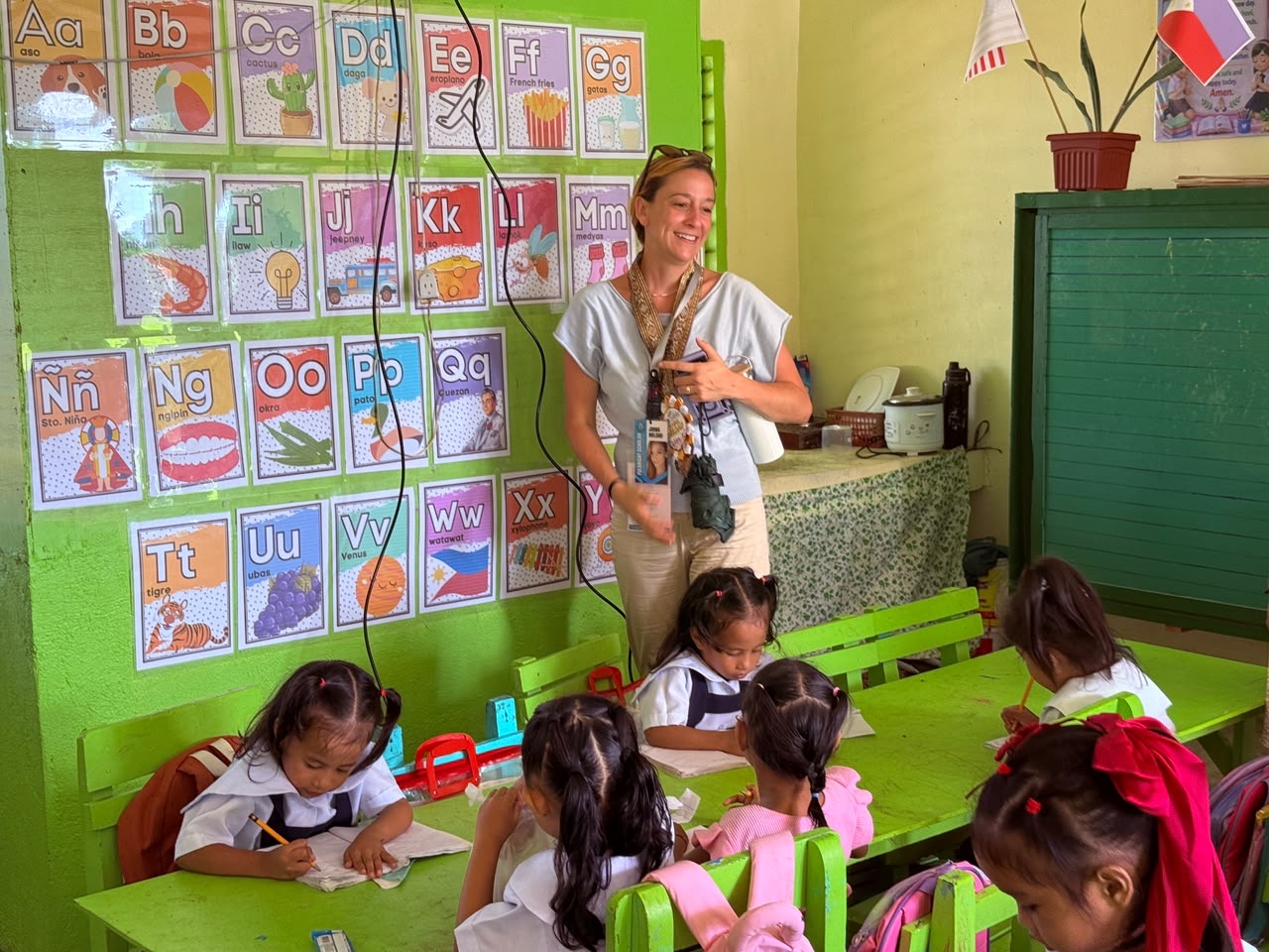 Johna Meldau teaching young students in a classroom with an English alphabet wall.
