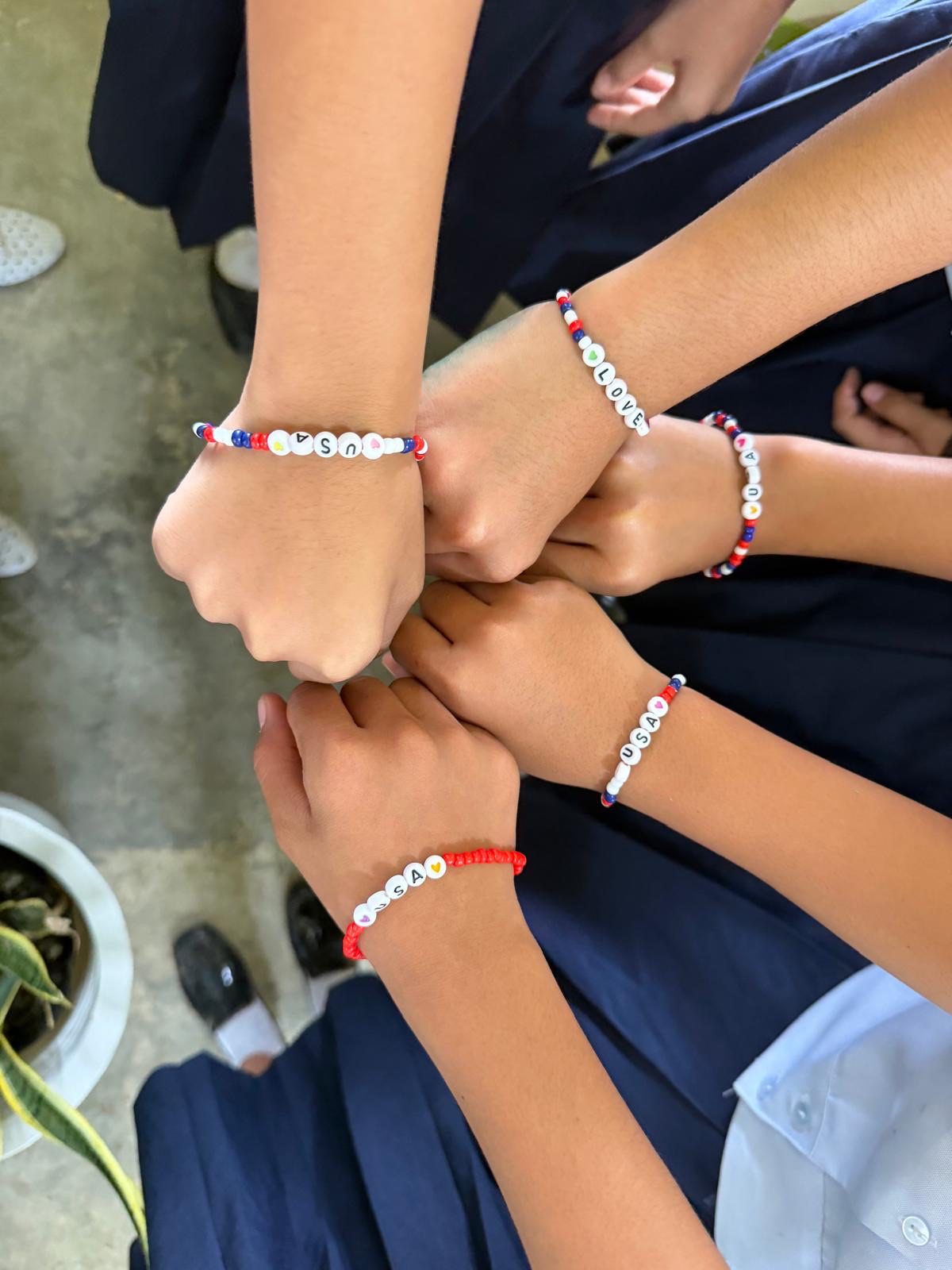 Students' wrists with beaded bracelets spelling USA and LOVE in red, white, and blue.