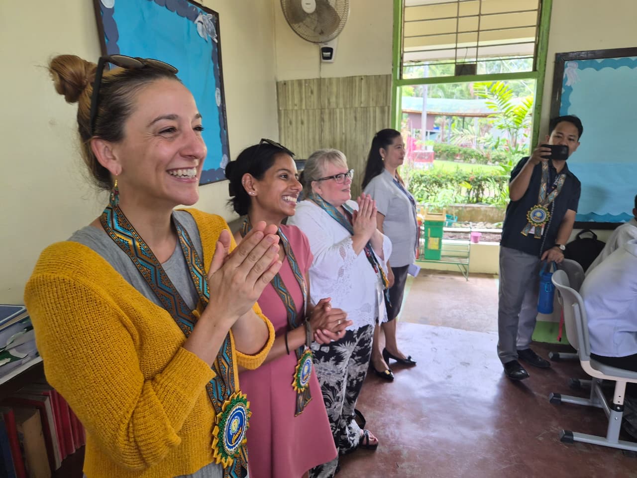 Fulbright teachers smiling and applauding while wearing ceremonial sashes.