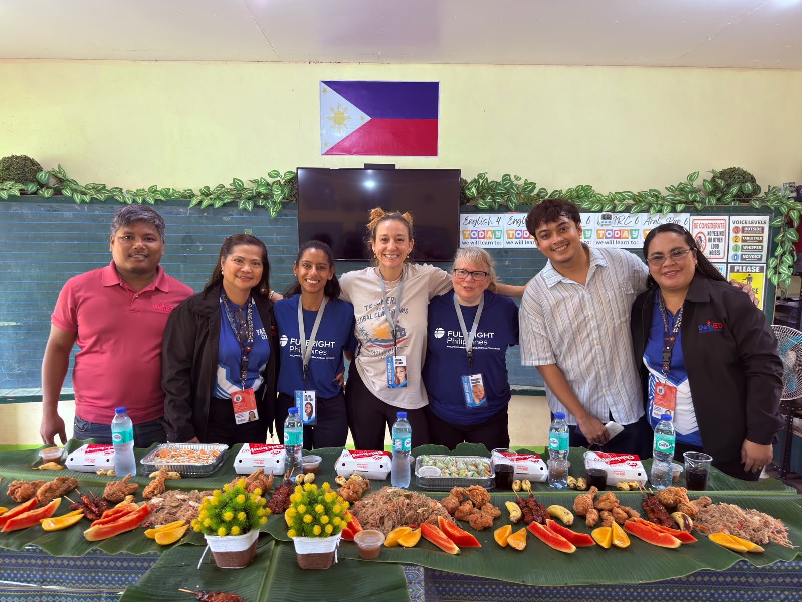 Educators standing behind a spread of Filipino dishes and fresh fruit.