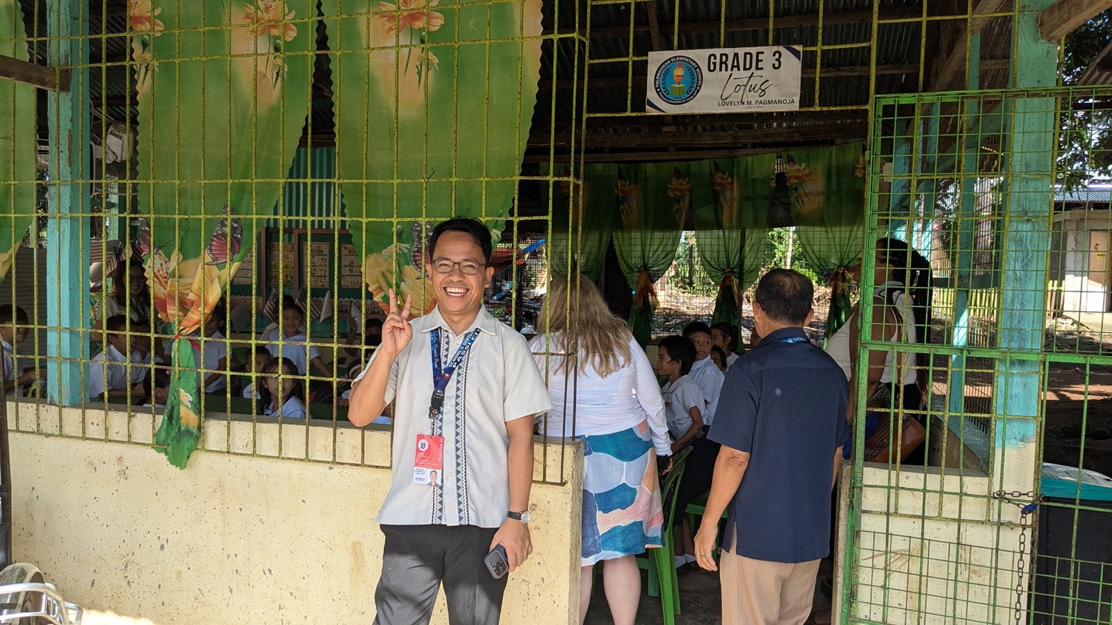 A Filipino teacher smiling at the gate of a Grade 3 classroom.