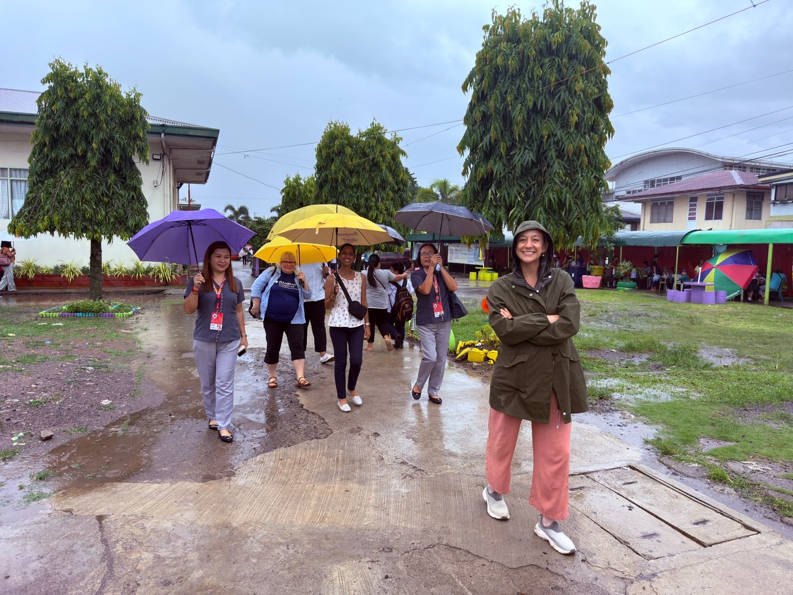 Johna Meldau and Filipino teachers with umbrellas on a rainy school campus.