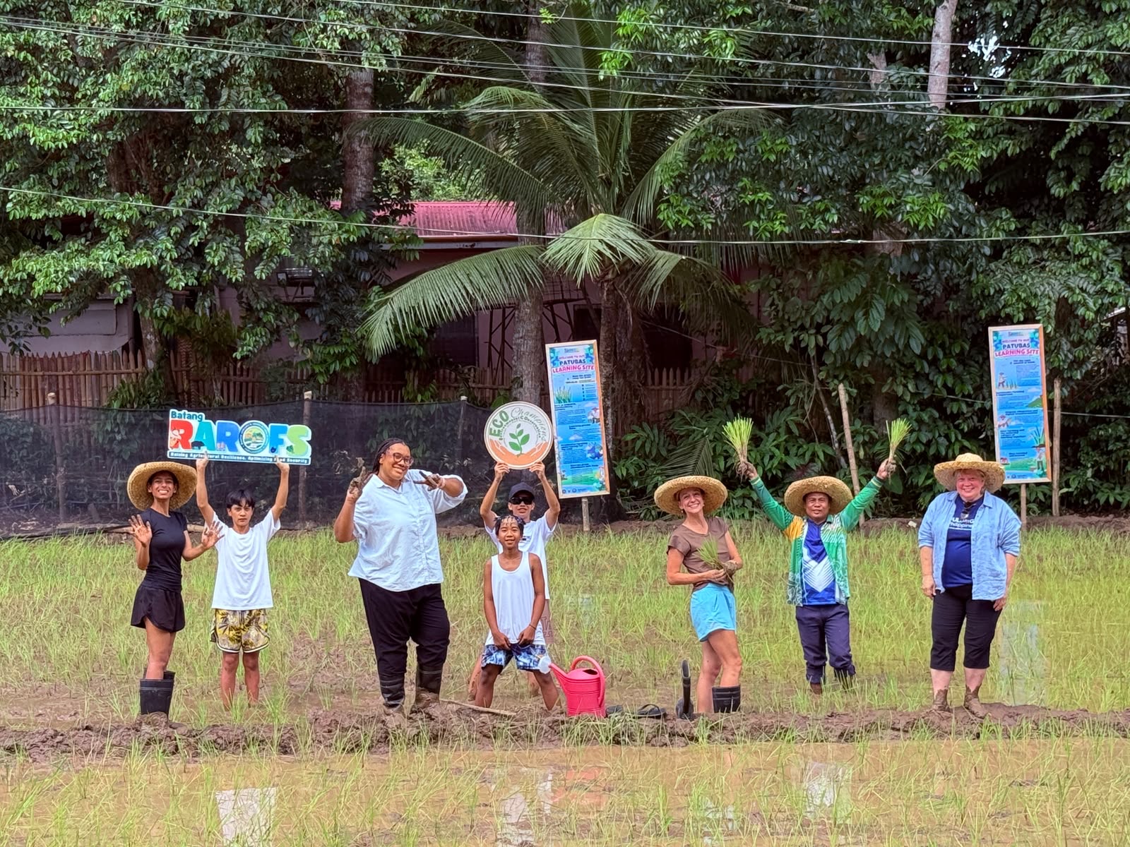 Fulbright teachers and students in a rice paddy holding eco-farming signs.