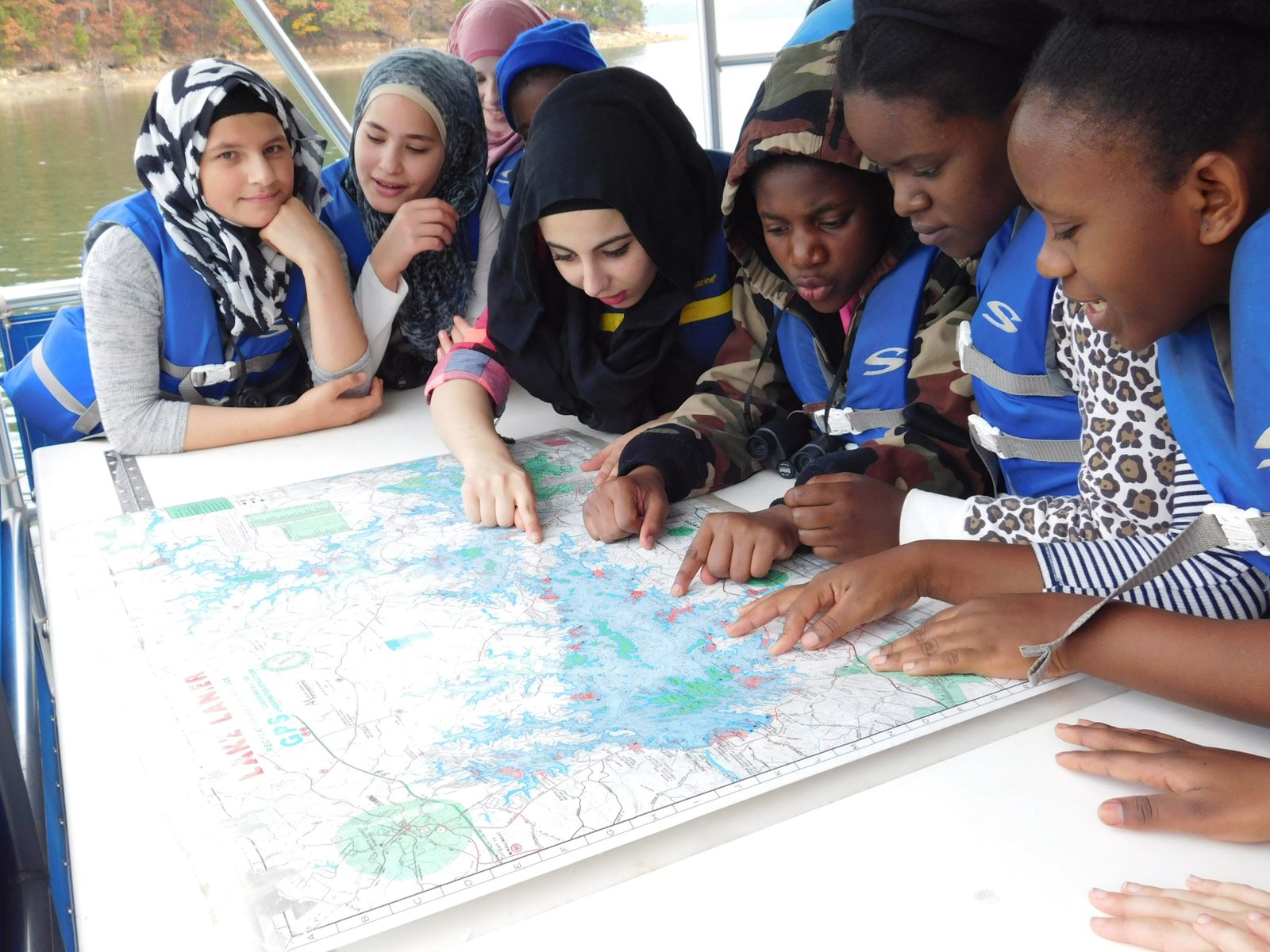 Students in life jackets studying a Lake Lanier map on a boat during a place-based learning trip