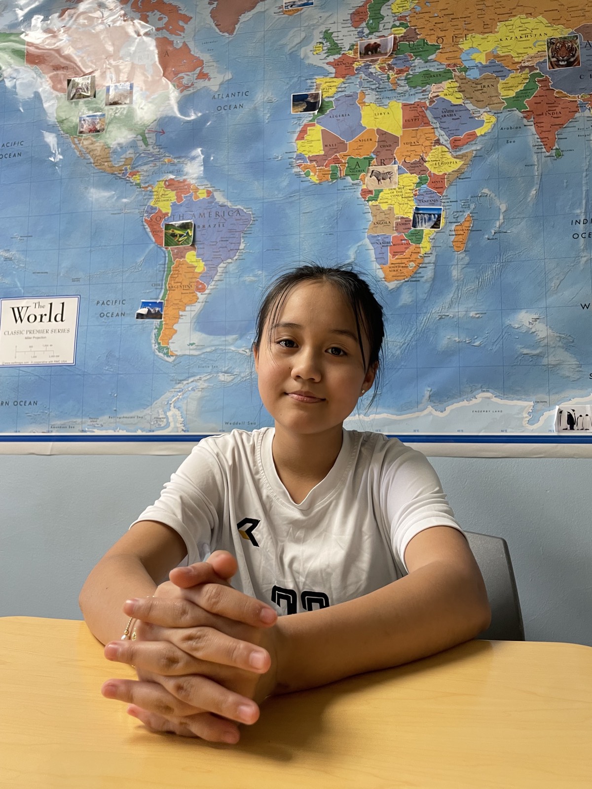 A student sits at a table in front of a large world map pinned with photographs